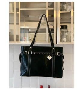 Detail of black glossy tote bag featuring a silver heart charm and metal buckle strap