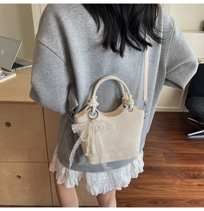 Détail du sac seau crème orné de nœuds en dentelle, perles et imprimé logo chic