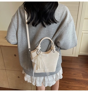 Sac seau beige avec nœud en dentelle et perles porté par un mannequin chez soi