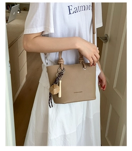 Detail of khaki lychee grain leather bucket bag with knotted handle and fashion logo