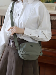 Olive green nylon saddle crossbody bag with adjustable strap worn by a female model