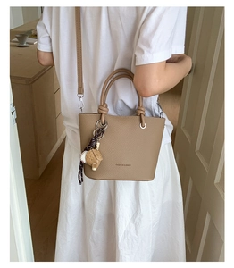 Close-up of litchi grain leather bucket bag with braided rope and cartoon charm decoration