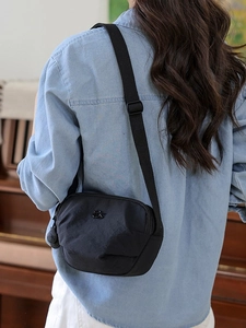 Minimalist black nylon saddle bag with round metal logo and wide adjustable strap