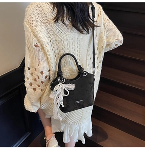 Détail du sac seau noir avec nœud en dentelle, breloque perle et logo sur escalier