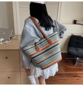 Multi-colored striped straw tote bag with brown leather handles worn by a model