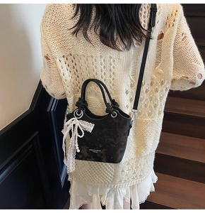 Vue détaillée du sac seau noir avec nœud en dentelle et pendentif perle porté par le mannequin