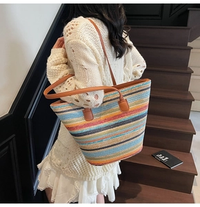 Detail of colorful woven straw tote featuring brown leather straps and multi-color stripes