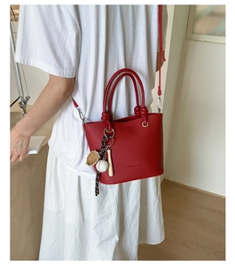 Detail of red pebbled leather handbag with baseball charm and knotted handle design