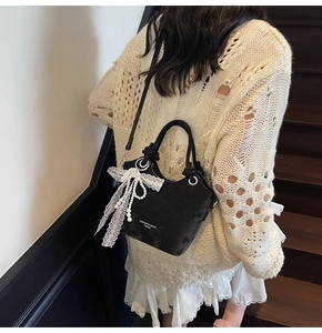 Détail du sac à bandoulière noir mat avec nœud en dentelle blanche et pendentif perle