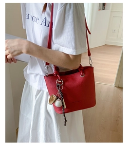 Detail of red bucket bag with litchi texture and unique baseball glove charm accessory