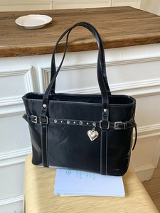 Glossy black tote bag with silver eyelet belt and heart pendant on a yellow stool