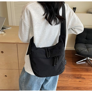 Detailed view of black nylon crossbody bag featuring woven logo label and zipper cord