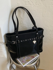 Glossy black tote bag with silver studs and heart charm on a stylish metal stool