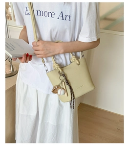 Détail du sac seau beige en cuir grainé avec breloques de baseball et bandoulière