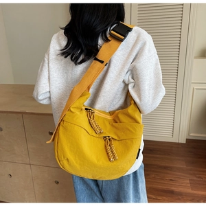 Detail view of bright yellow crossbody dumpling bag showing wide strap and buckle on model