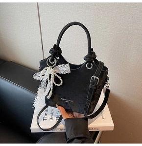 Gros plan du sac seau en velours noir avec nœud en dentelle, breloque perle et détails