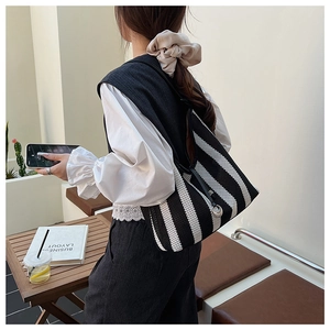 Detail view of woven striped tote bag with black leather shoulder strap and metal buckle
