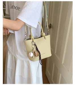 Detail of beige lychee leather bucket bag featuring a baseball charm and striped ribbon