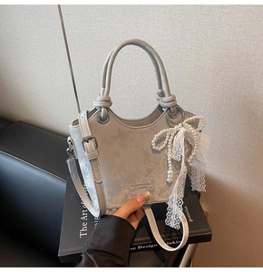 Vue détaillée du sac seau en daim gris clair avec un nœud en perles et un charme en dentelle