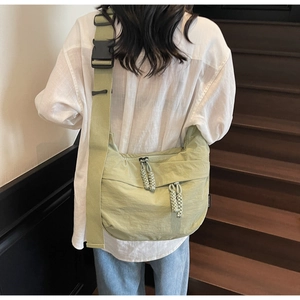 Detail showing light green dumpling bag with woven rope zippers and wide shoulder strap