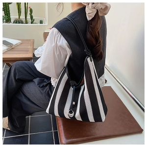 Black and white striped mesh tote bag with leather straps worn by a model in a bright room