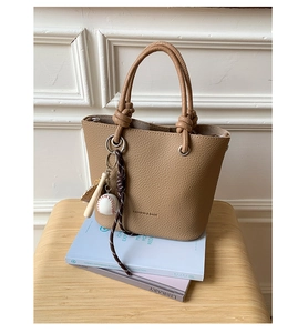 Detail of light brown lychee grain bucket bag with baseball charms on a stack of books