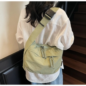 Detail of light green nylon crossbody bag with black wide strap and woven zip puller