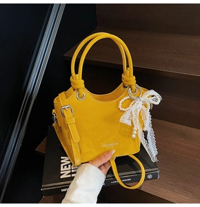 Détail d'un sac seau jaune vif en cuir synthétique avec breloques en dentelle et perles