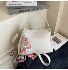 Détail du sac seau crème avec texture litchi et pendentif arc-en-ciel tenu par la main