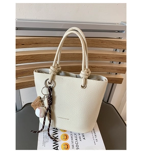Close-up of cream white bucket bag with pebble leather texture and baseball bag charm