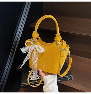 Détail d'un sac seau jaune avec breloque perle et dentelle sur escalier en bois