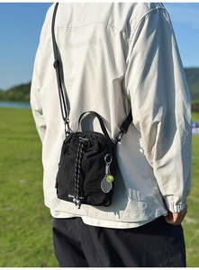 Outdoor view of a black nylon drawstring crossbody bag with a tennis racket keychain detail