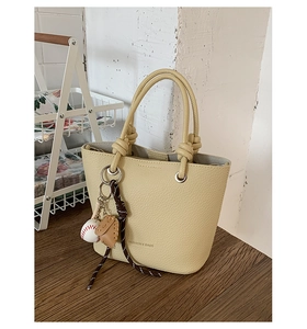 Detail view of lychee texture bucket bag with baseball charm and knotted handle design