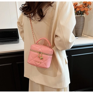 Mini borsa trapuntata rosa con catena dorata e ciondolo a cuore in un ambiente lifestyle