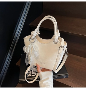 Détail du sac cabas blanc avec nœud en perles et boucles métalliques sur escalier en bois