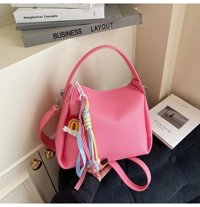 Vue détaillée d'un sac seau en cuir grainé rose avec un charme arc-en-ciel et pompons