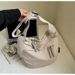Close-up of cream white nylon crescent bag with wide strap and large black buckle detail