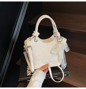 Détail d'un sac seau blanc avec poignée à nœud et breloque en dentelle de perles