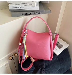 Détail du sac seau en cuir litchi rose avec breloque tressée et bandoulière amovible