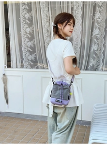 Detail of lavender and gray drawstring crossbody bag with neon yellow charm and adjustable strap