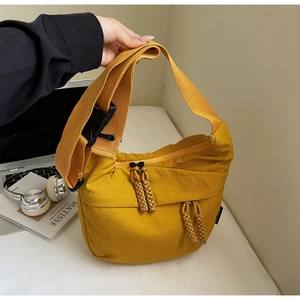 Detail of yellow nylon crossbody bag featuring wide strap, buckle and rope zipper pulls