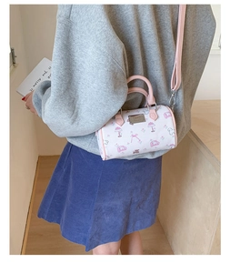 Close-up of mini white cylinder bag featuring pink cartoon prints and metal nameplate
