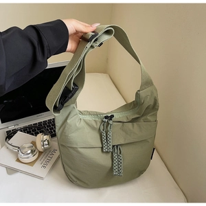 Detailed view of sage green nylon crossbody bag with dual zippers and woven pullers
