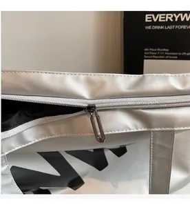 Detail of a smooth silver satin tote bag showing a large black letter print and metal zipper
