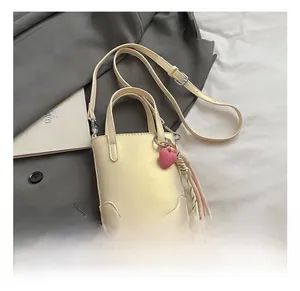 Détail du sac seau crème avec breloque cœur rose et pompon posé sur un blazer gris