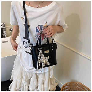 Detail of black crocodile texture bucket bag with silver star charm and tassel on a model