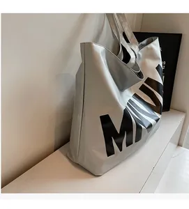 Close-up of a silver tote bag showing glossy textured fabric and black letter print