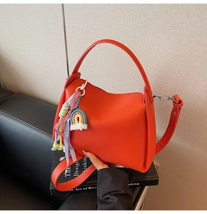 Détail d'un sac seau orange en cuir grainé avec charm arc-en-ciel et ruban à carreaux