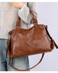 Detail of a brown leather tote bag with cross stitching and adjustable strap