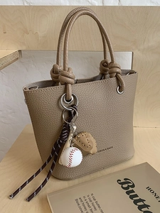 Minimalist khaki leather bucket bag with knot handle and baseball charm on display